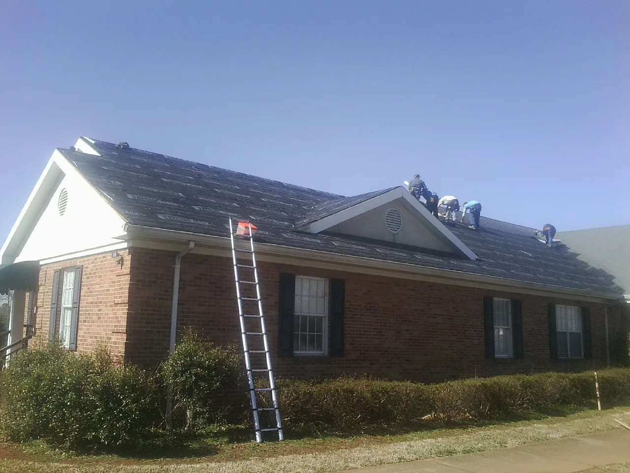 Crew tearing shingles off a brick ranch roof with a ladder set — Metal Roof Repair work by our crew in Fort Knox