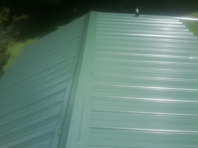 New green metal panels meeting at the ridge of a roof — Flat Roof Repair work by our crew in Fort Knox