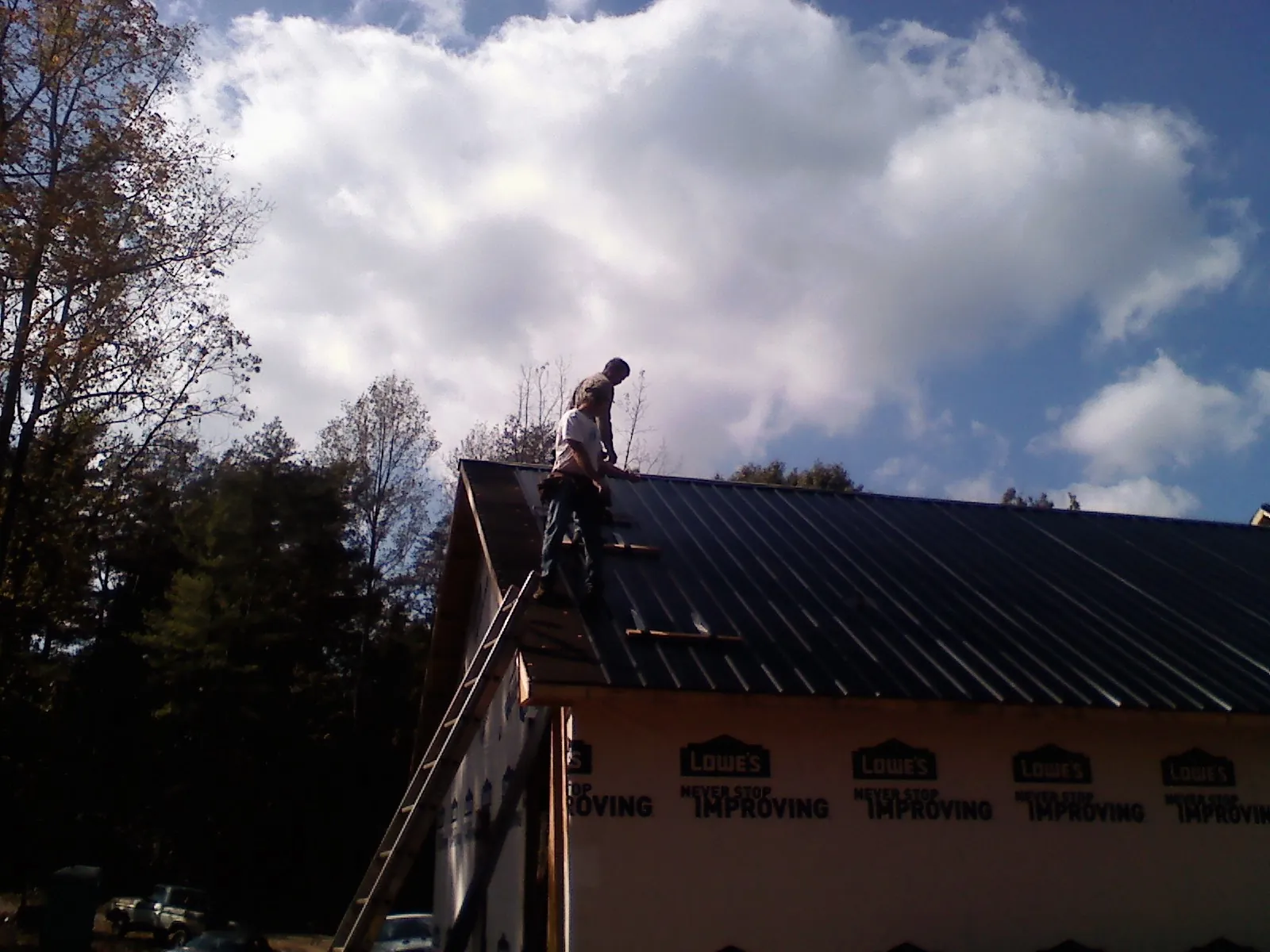 Roofer fastening dark metal panels high against a cloudy sky, from a Roof Inspection job in Fort Knox