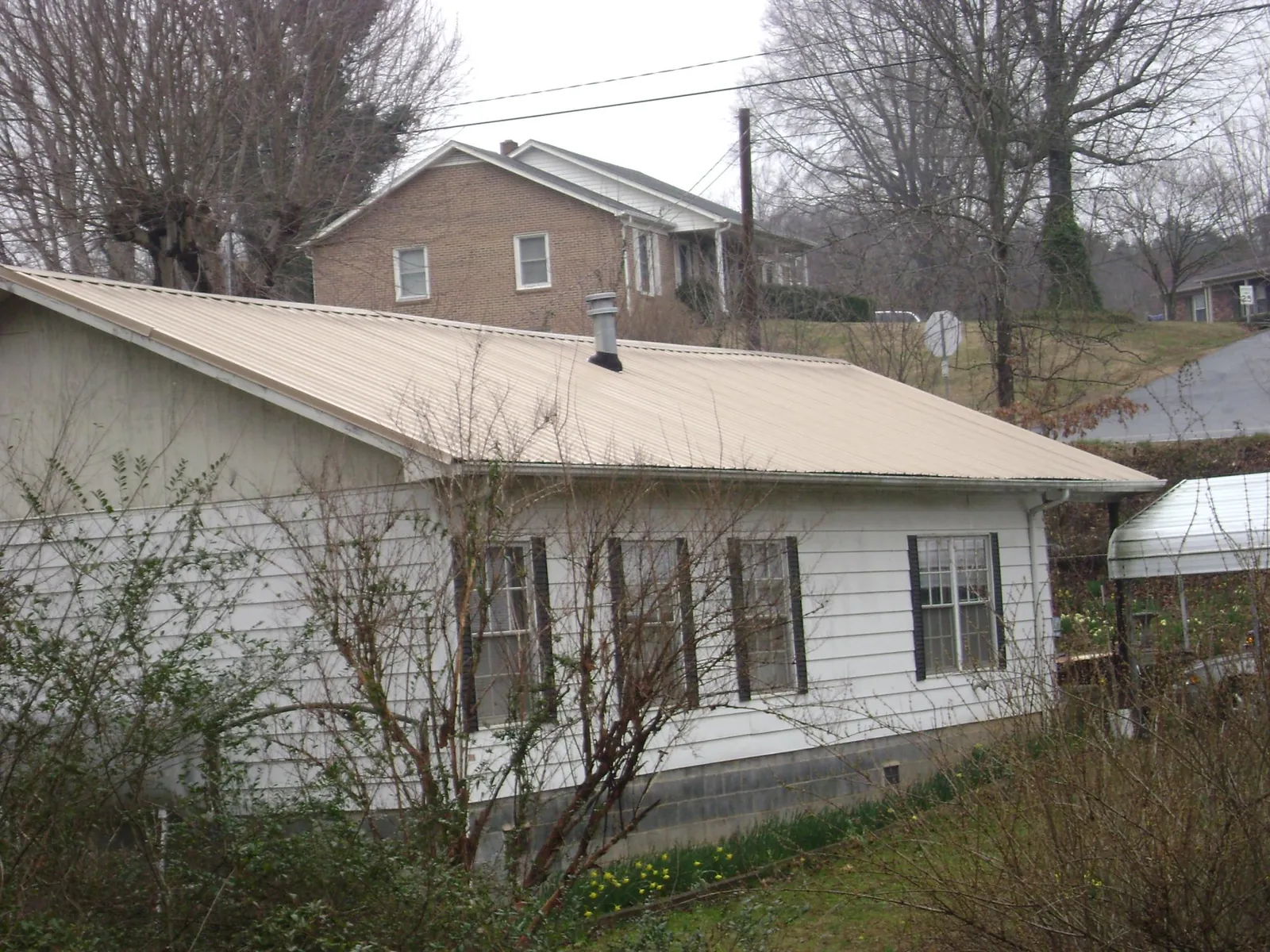 Tan metal roof on a white sided house set into a hillside — Commercial Roofing by Roofing Brothers in Fort Knox